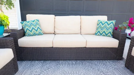 Stylish outdoor couch with cream cushions and patterned throw pillows on a decorative rug.