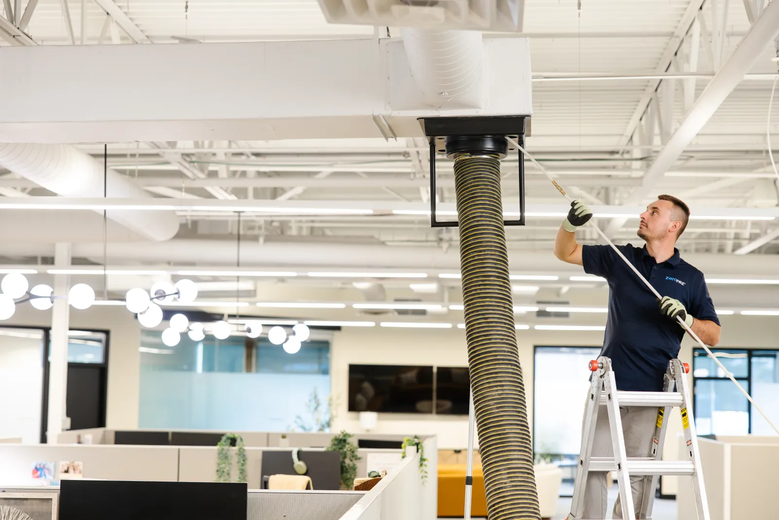 technician with tool to clean air duct system in office building