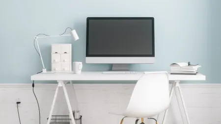 Minimalist home office desk with computer, white chair, lamp, books, and Zerorez logo on blue wall